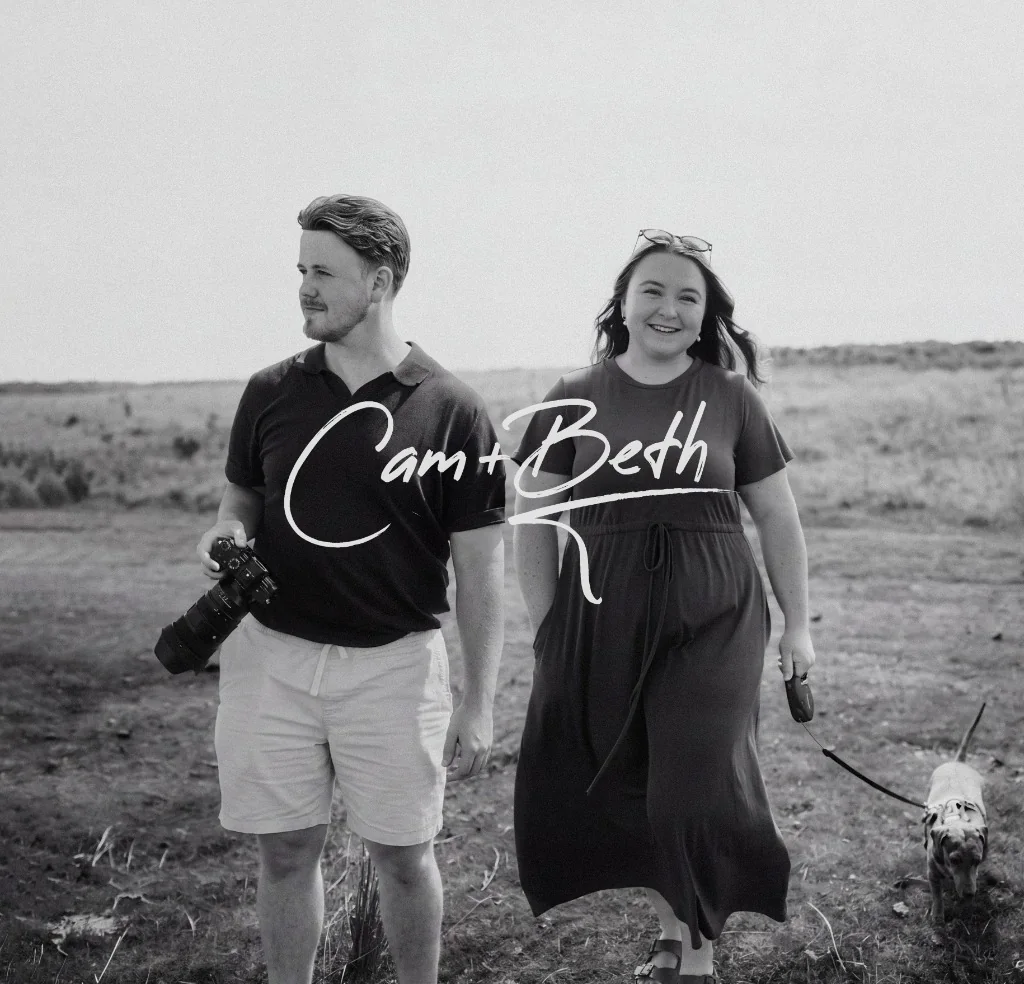 Cam and Beth walking together in a field, Cam holding a camera
