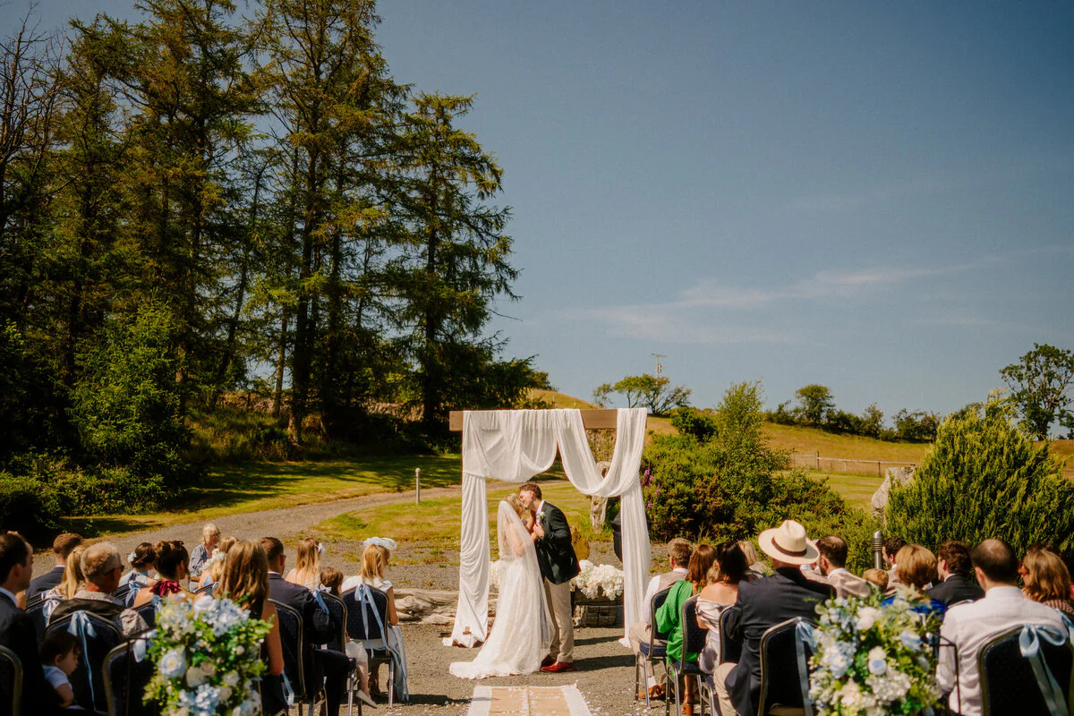 Ca106253 Edit Outdoor wedding ceremony beneath tall trees, captured by a South Wales wedding photographer.