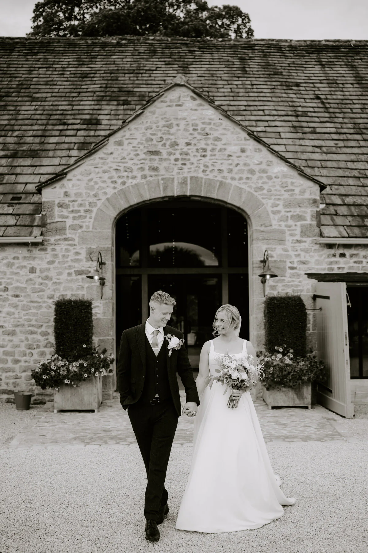 Dsc07177 Black and white photograph of newlyweds walking outside a stone barn wedding venue.