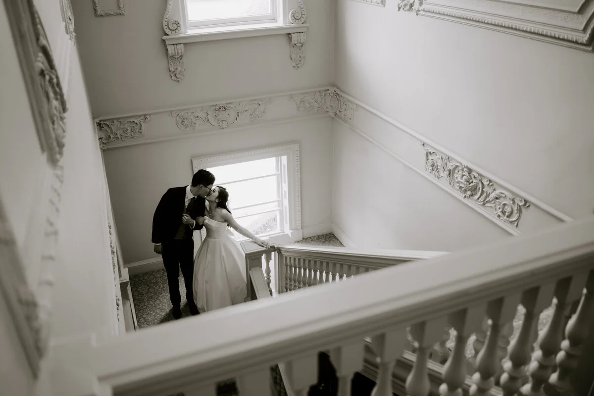 A7r06716 2 Black and white photograph of newlyweds sharing a kiss on an elegant staircase.