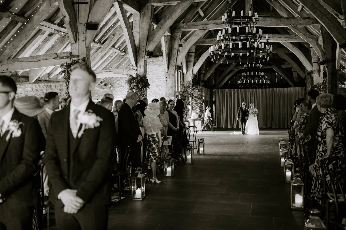 Dsc04876 2 Wide black and white view of a lantern-lined barn wedding ceremony beneath timber beams.