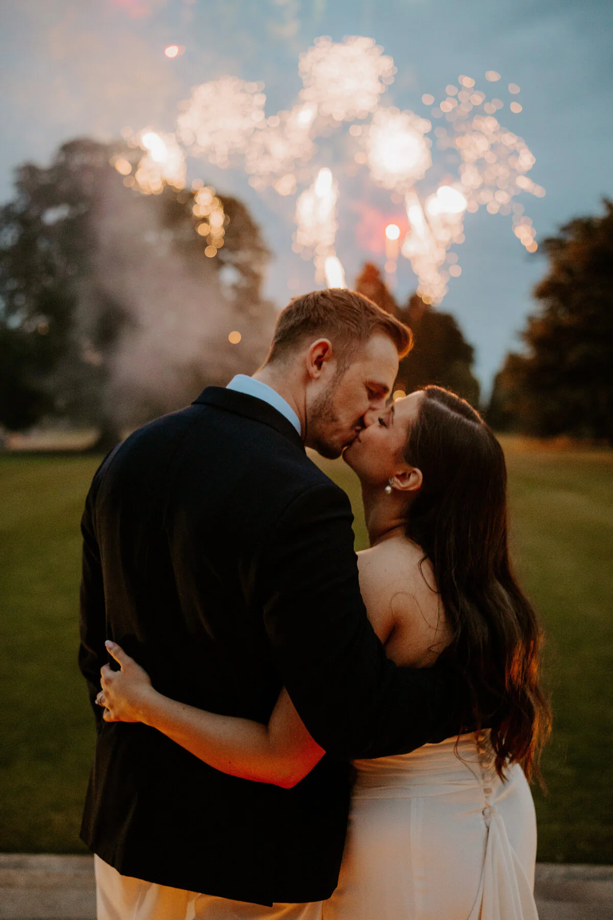 Dsc08272 1 Bride and groom kissing beneath a firework display at night.