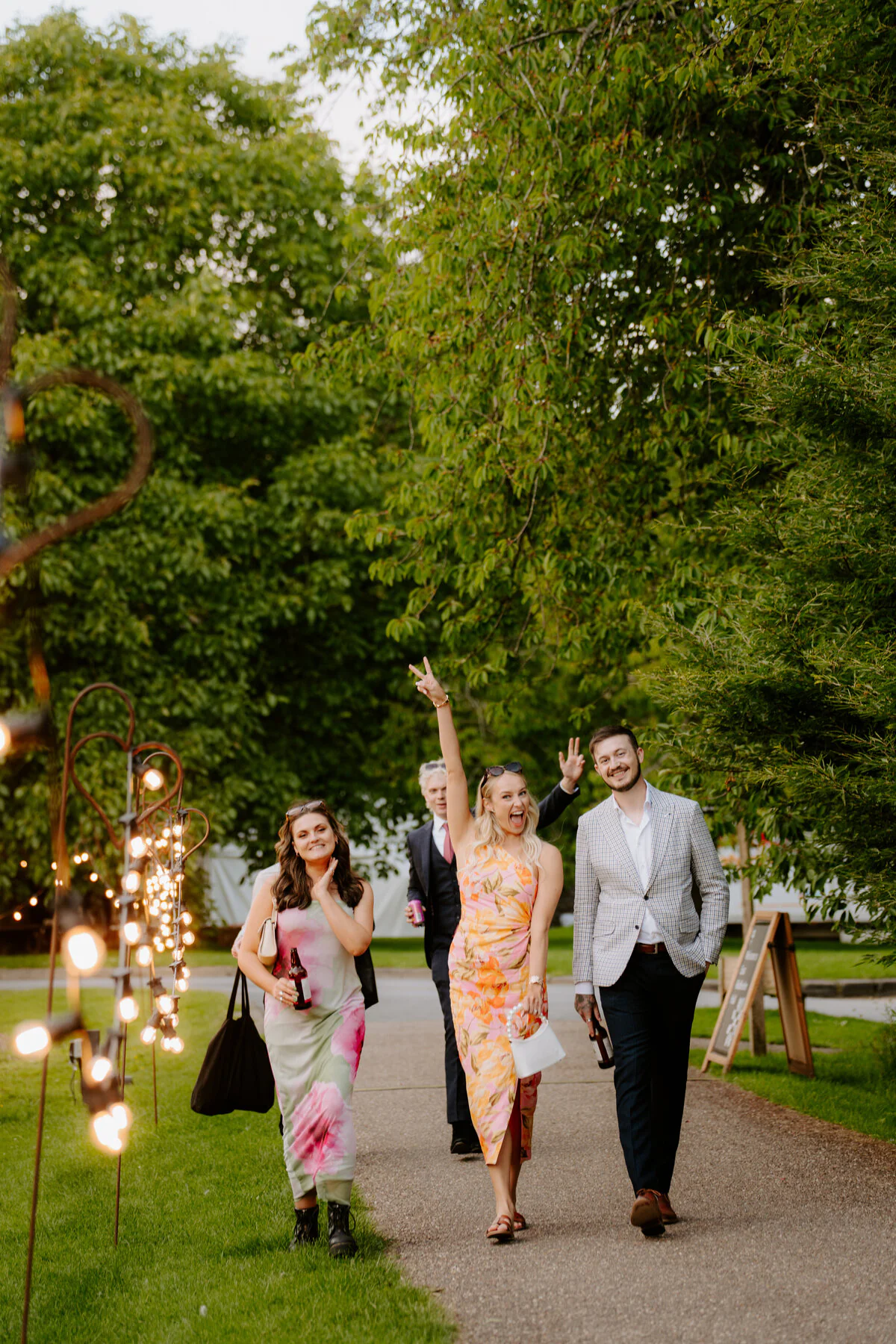 Dsc08165 Wedding guests in colourful dresses walking a festoon-lit path in the evening.