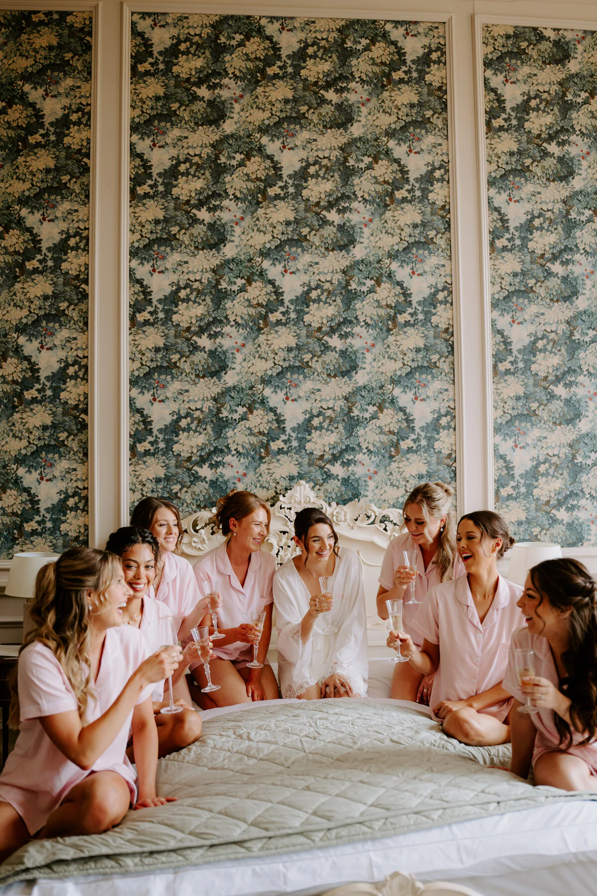 Dsc01888 Bride in a white robe with bridesmaids in pink pyjamas on a bed with champagne.