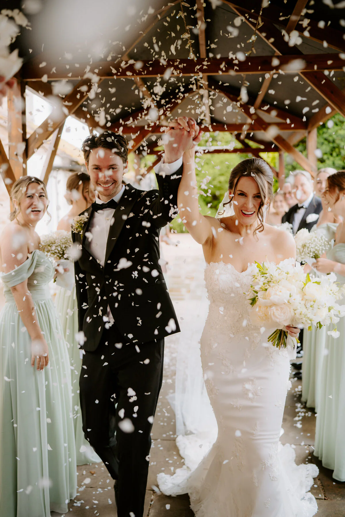 Charlie And Peter 306 Confetti throw as Charlie and Peter leave their wooden wedding pavilion with sage-green bridesmaids.