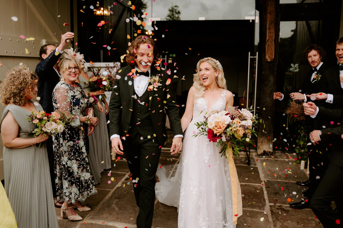 Dsc03588 Confetti thrown outside a barn entrance over a lace gown and dark-green three-piece suit.