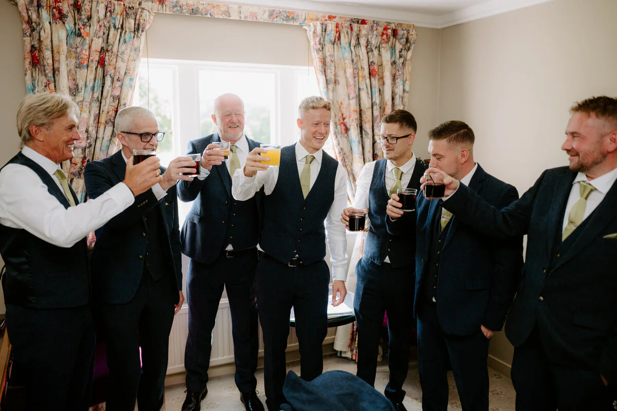 Dsc04091 Groomsmen in navy suits toasting with drinks in a cottage drawing room.