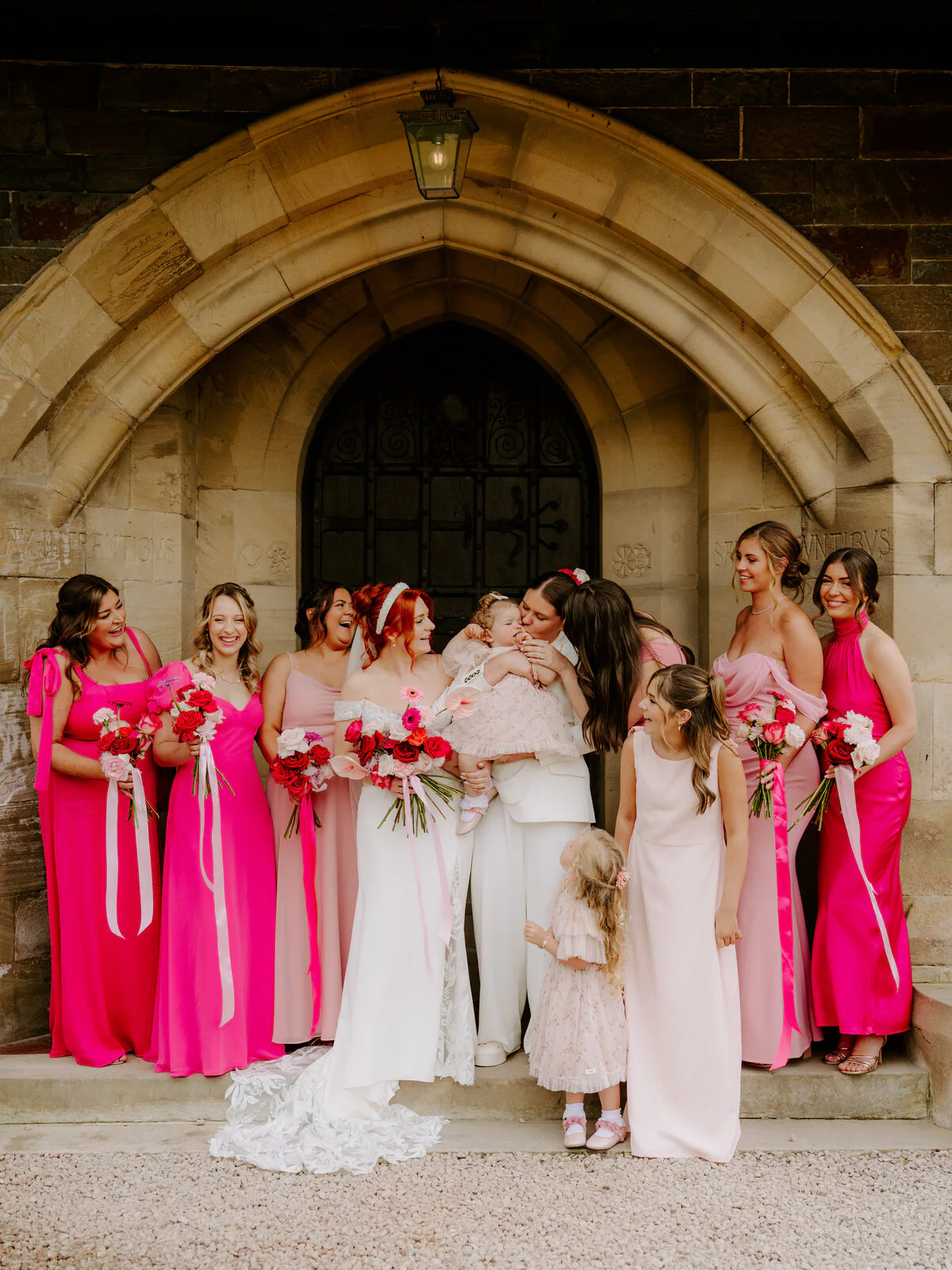 Dsc06066 Two brides with their bridal party in pink dresses outside a stone church archway.