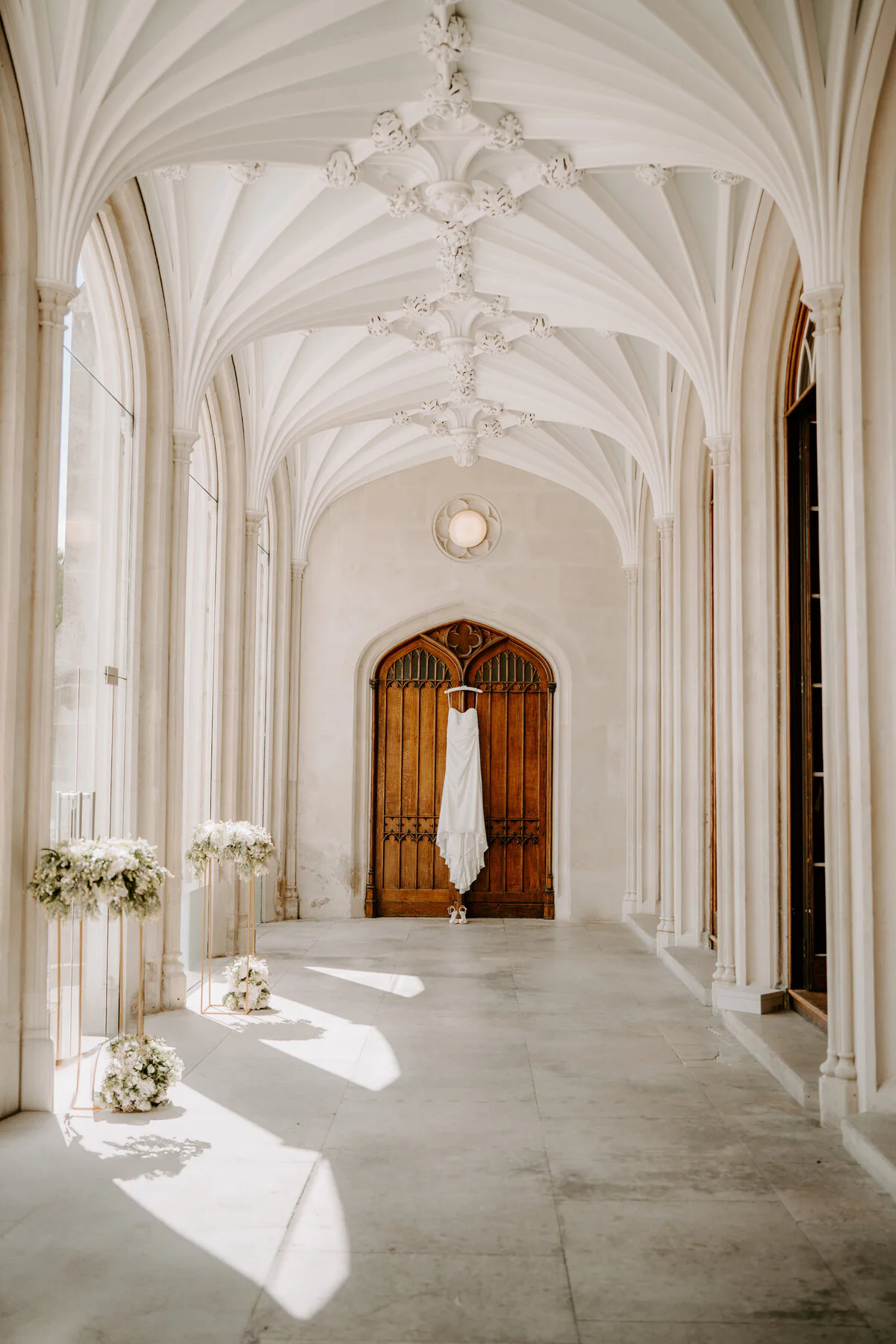 Dsc01819 Wedding dress hanging on a gothic wooden door in a white stone cloister corridor.