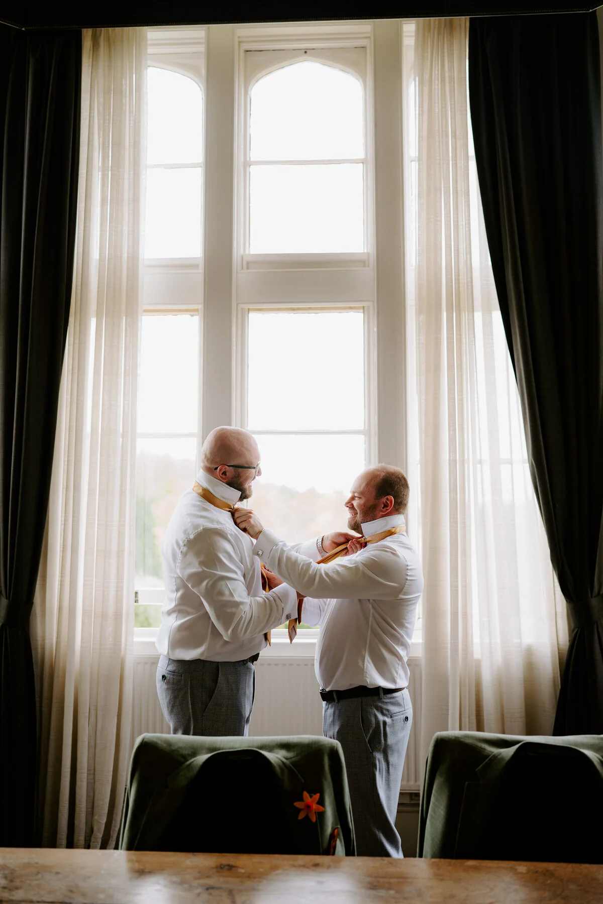 Dsc05098 Best man and groom in gold ties getting ready beside a tall window.
