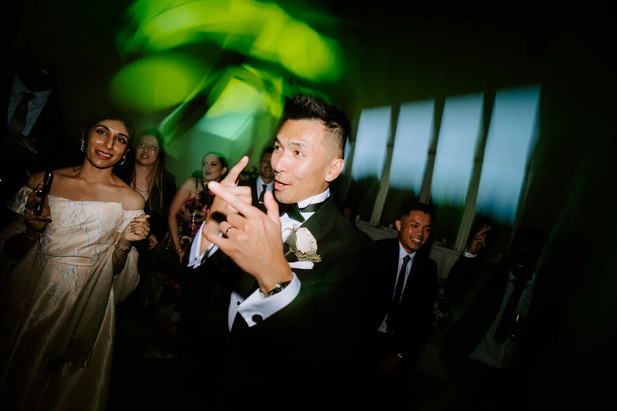 Dsc08272 5 Groom dancing and pointing at the camera under green lights with the bride behind him.
