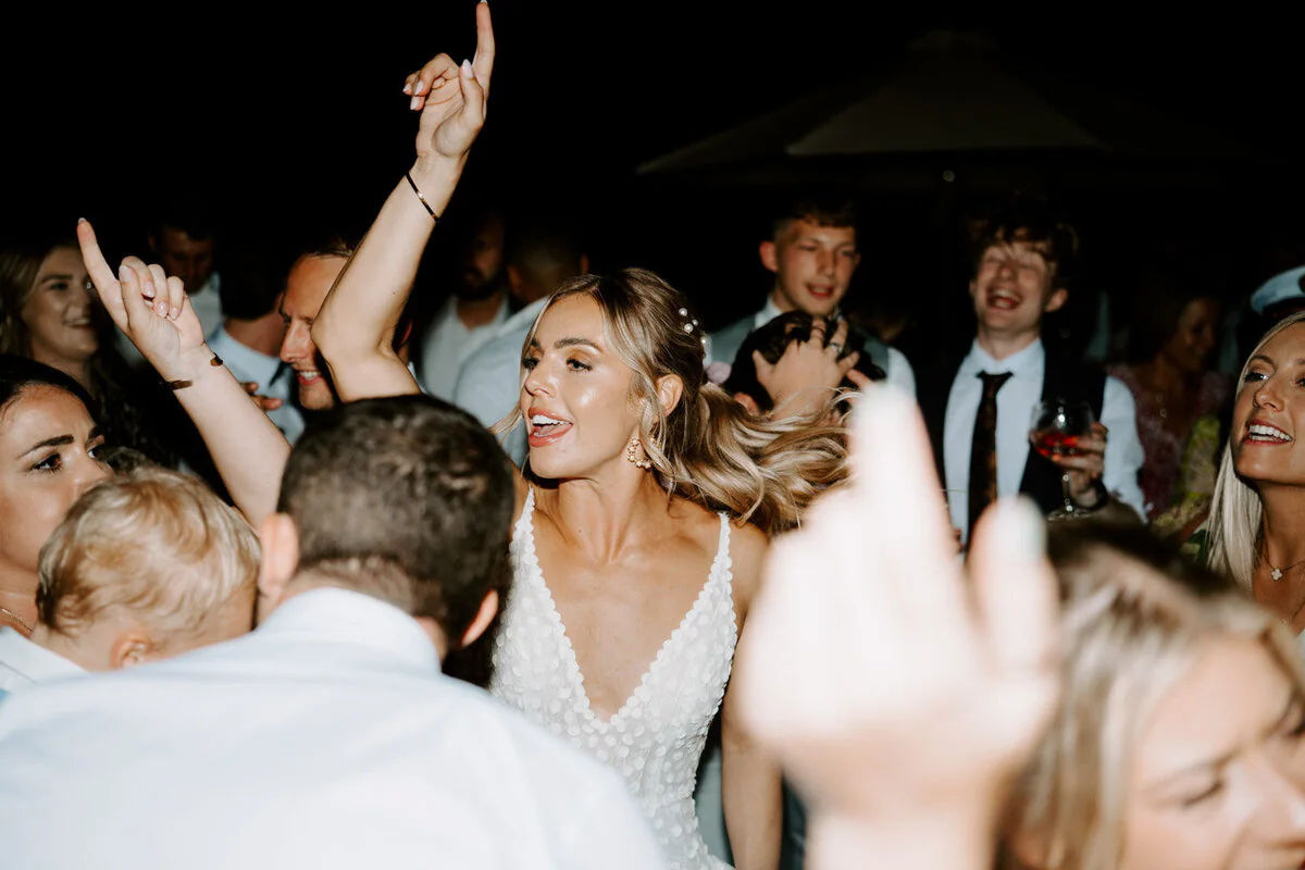 Dsc01338 10 Bride dancing with her arms raised among guests on the dance floor at night.