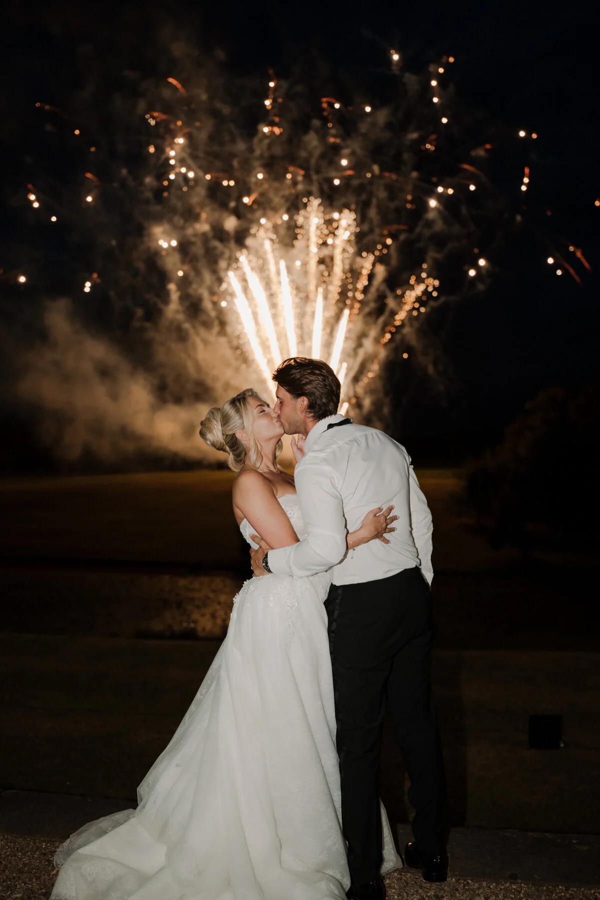 Ca104191 Edit Bride and groom kissing at night in front of a golden firework display.