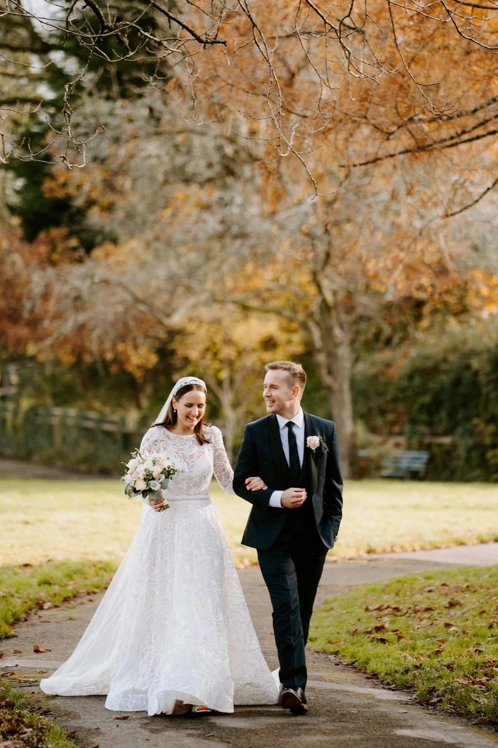 Ruth and Rhodri walking arm in arm along a path beneath colourful autumn trees